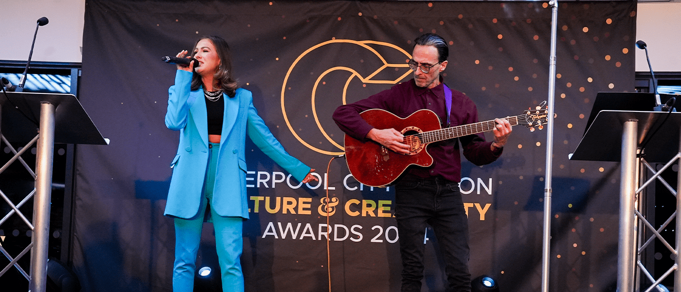 woman in blue suit and man with guitar on stage