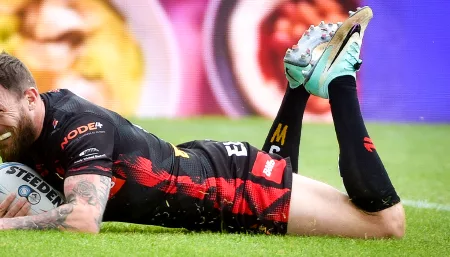 A rugby player, a man, is lying on the ground with his hands resting on his knees, showing signs of exhaustion.