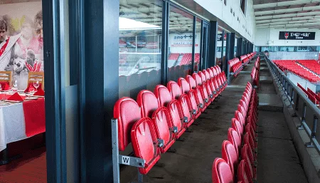A stadium box room featuring red chairs arranged in stands, creating a vibrant dining atmosphere for guests.