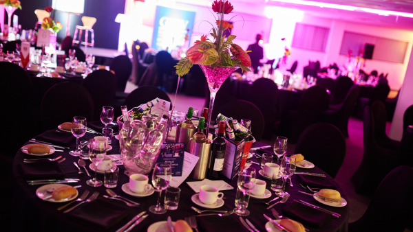 A beautifully arranged dinner table illuminated by soft purple lighting, creating an inviting atmosphere for guests.